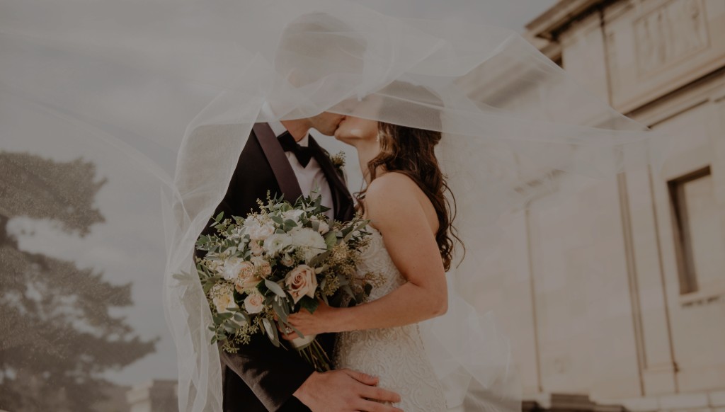 Bride and groom kissing under a flowing veil